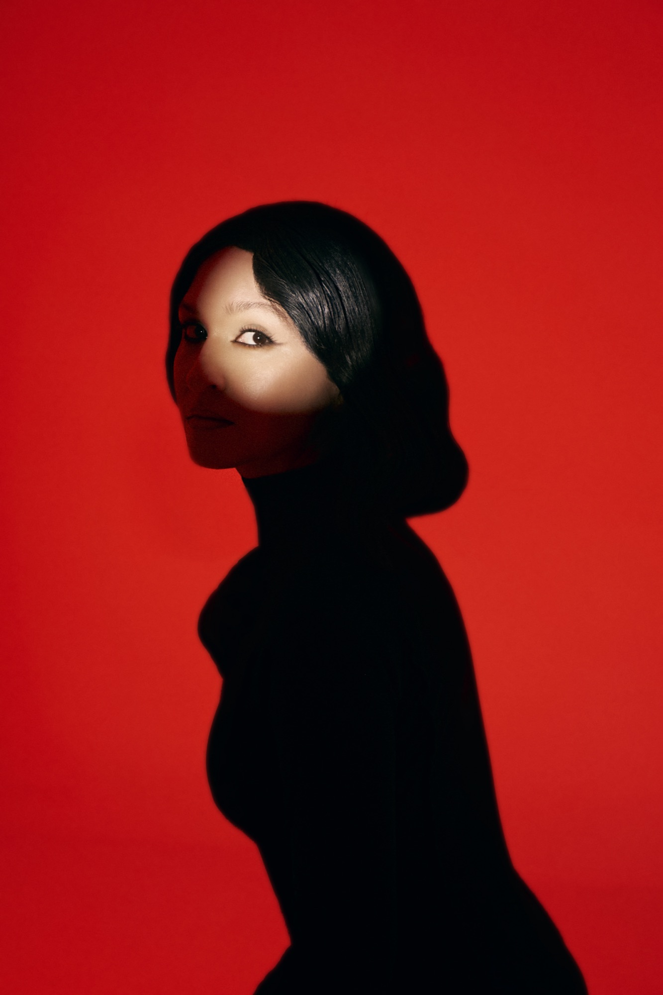 AYGYUL in black against a red wall, looking over her shoulder